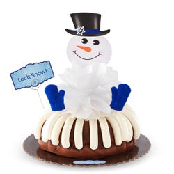A decorated bundt cake with a snowman with a carrot nose and 2 knit mittens. A card is on the cake that says Let It Snow!.
